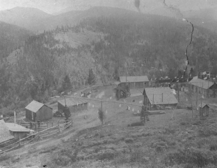 Historic black-and-white photograph of Bell's Camp, a mining settlement of wooden cabins on a forested Colorado mountainside